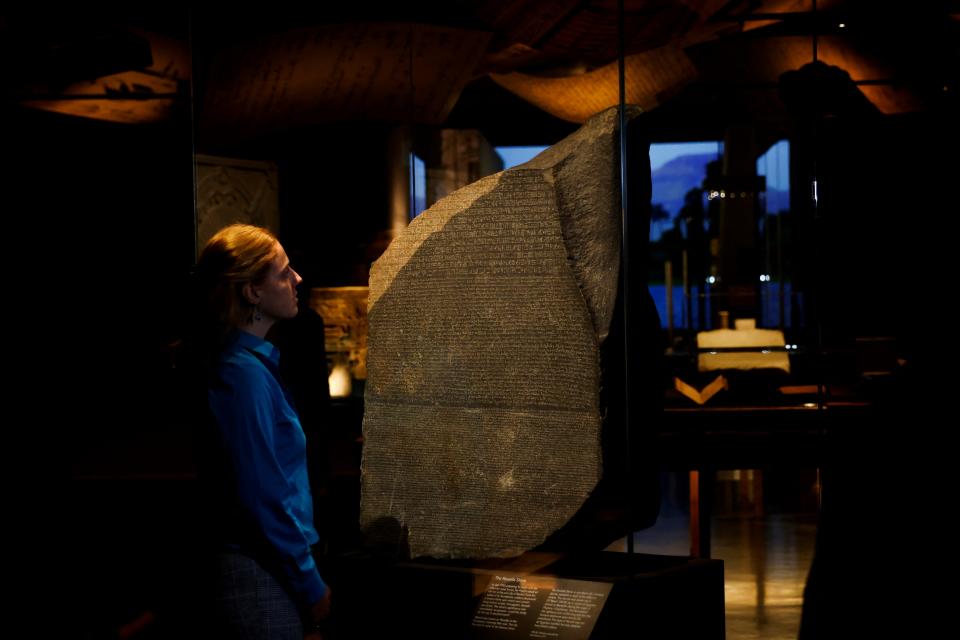 A member of staff looks at The Rosetta Stone displayed for the exhibition 