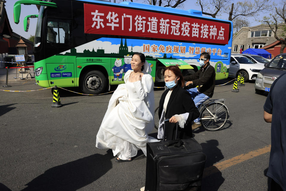 A woman in a wedding gown passes a bus offering free coronavirus vaccinations outside the Forbidden City in Beijing on Wednesday, April 14, 2021. China's success at controlling COVID-19 has resulted in a population that has seemed almost reluctant to get vaccinated. Now it is accelerating its inoculation campaign by offering incentives — free eggs, store coupons and discounts on groceries and merchandise — to those getting a shot. ​(AP Photo/Ng Han Guan)