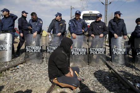 A migrant sits next to the riot police as other migrants block the railway track at the Greek-Macedonian border, near the village of Idomeni, Greece March 3, 2016. REUTERS/Marko Djurica