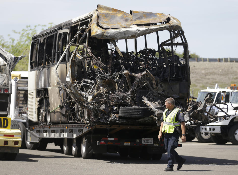 A California Highway Patrol officer walks past the charred remains of a tour bus at a CalTrans maintenance station in Willows, Calif., Friday, April 11, 2014. At least ten people were killed and dozens injured in the fiery crash on Thursday, April 10, between a FedEx truck and a bus carrying high school students on a visit to a Northern California college. (AP Photo/Jeff Chiu)