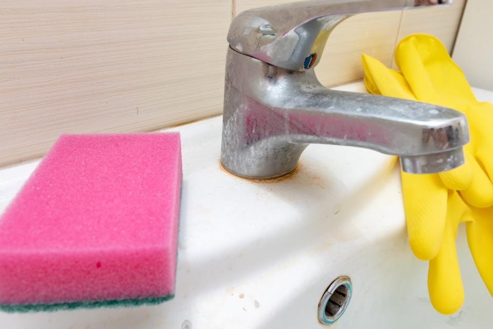 Sponge and gloves for washing dirty faucet with limescale, calcified water tap with lime scale on washbowl in bathroom, house cleaning concept.