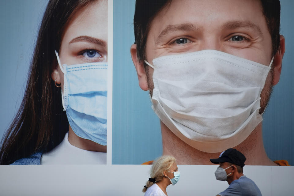 People wearing protective face masks walk by a billboard raising the awareness of wearing face masks and washing hands following government measures to help stop the spread of the coronavirus, in Ramat Gan, near Tel Aviv, Israel, Thursday, July 16, 2020. Israel reached a new daily record of confirmed coronavirus cases on Thursday as the government discussed renewed lockdown measures to contain the growing outbreak. (AP Photo/Oded Balilty)