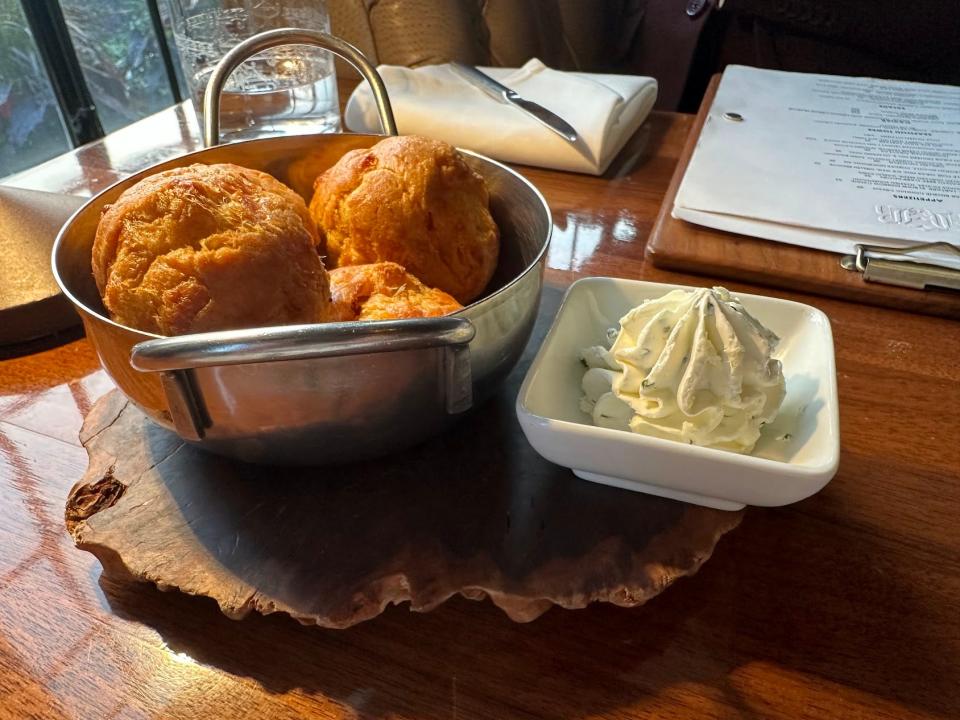 A silver bowl with gougères and a while ramekin filled with whipped chive butter.