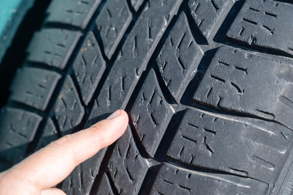 A close-up image of a finger pointing at the wear pattern on a car tire's tread