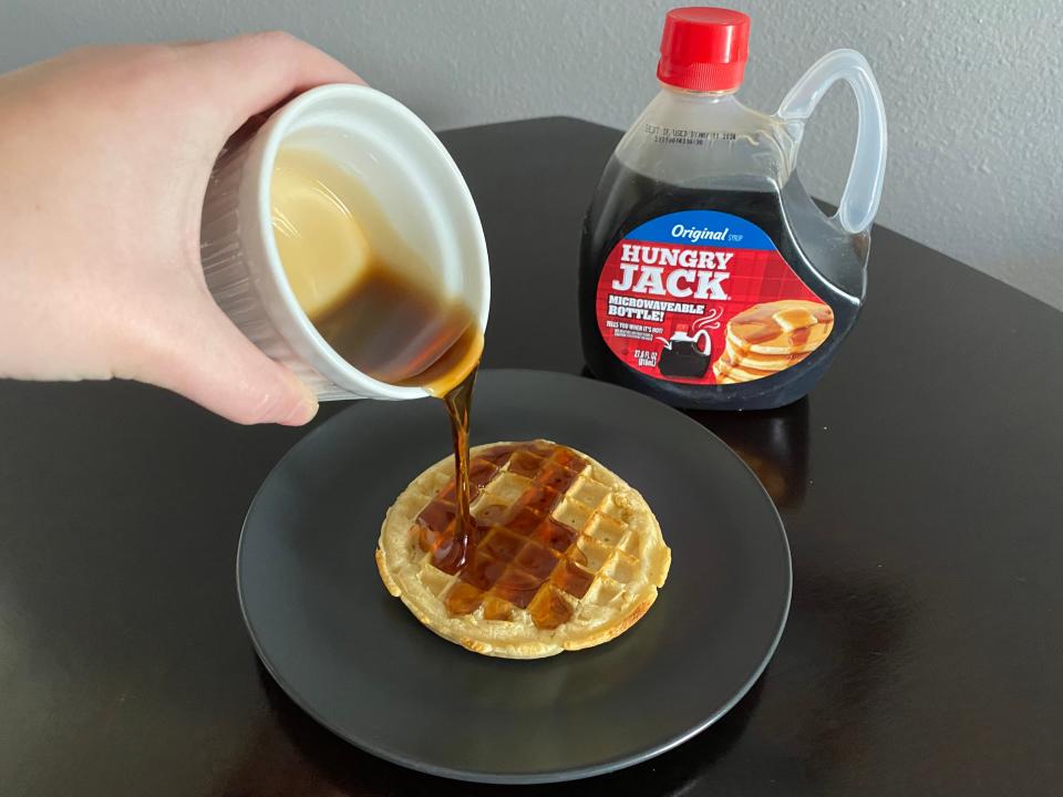 hand pouring white ramekin of hungry jack syrup over a frozen waffle