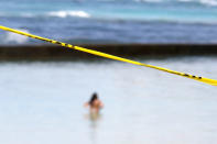 Police tape closes off Waikiki Beach as a woman swims in Honolulu on Saturday, March 28, 2020. Like many cities across the world, Honolulu came to an eerie standstill this weekend as the coronavirus pandemic spread throughout the islands. But Hawaii officials went beyond the standard stay-at-home orders and effectively flipped the switch on the state's tourism-fueled economic engine in a bid to slow the spread of the virus. As of Thursday, anyone arriving in Hawaii must undergo a mandatory 14-day self-quarantine. The unprecedented move dramatically reduced the number of people on beaches, in city parks and on country roads where many people rely on tourism to pay for the high cost of living in Hawaii. (AP Photo/Caleb Jones)