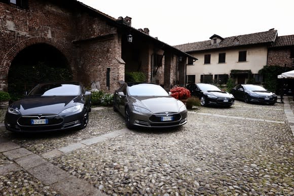 Four Tesla Model S sedans parked outside a stone building..