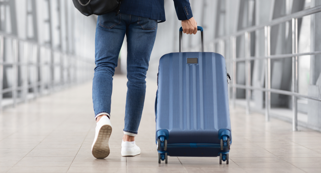 luggageman pulling blue suitcase through airport wearing jeans and white sneakers