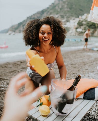 woman looking into camera, holding out bottle of SPF to extended hand in foreground