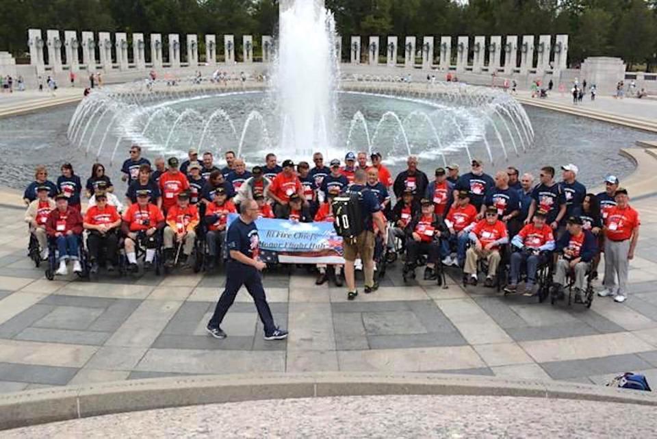  Chief George Farrell, Chairman of the RI Honor Flight program, walks in front of one of his groups posing for a group photo at the World War II Memorial.