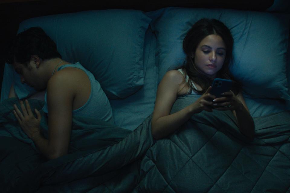 As Craig (Nat Wolff) sleeps, his fiancée Patti (right, Aimee Carrero) answers a late night text from Regus Patoff, the odd new boss at Craig's company.