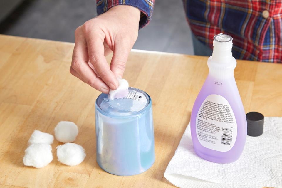 Woman uses nail polish remover on a cotton ball to remove a sticker on a candle jar.