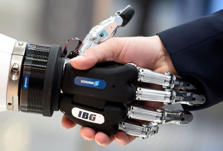 A visitor shakes hands with a humanoid robot at the booth of IBG at Hannover Messe, the trade fair in Hanover, Germany, April 23, 2018. REUTERS/Fabian Bimmer