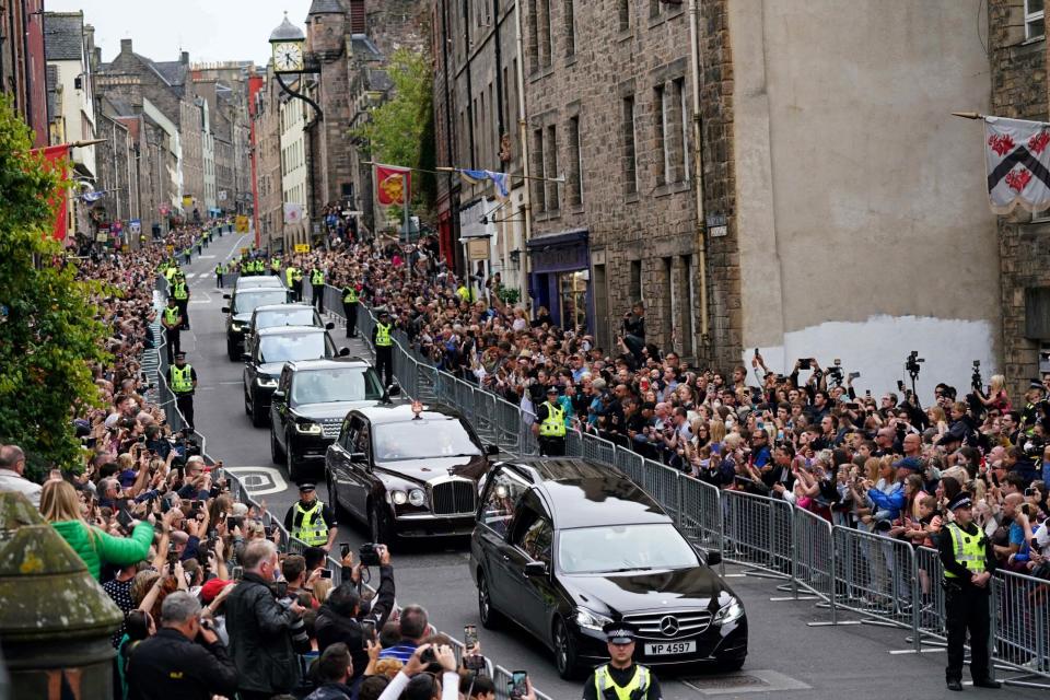 Members of the public stand on Cannongate to watch the hearse carrying the coffin of Queen Elizabeth II, draped in the Royal Standard of Scotland, as it is driven through Edinburgh towards the Palace of Holyroodhouse, on September 11, 2022. - The coffin carrying the body of Queen Elizabeth II left her beloved Balmoral Castle on Sunday, beginning a six-hour journey to the Scottish capital of Edinburgh. (Photo by Jacob King / AFP) (Photo by JACOB KING/AFP via Getty Images)