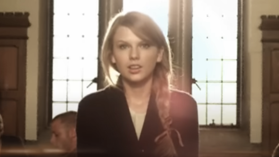 Woman resembling Taylor Swift in a courtroom setting, wearing a dark jacket and a braid