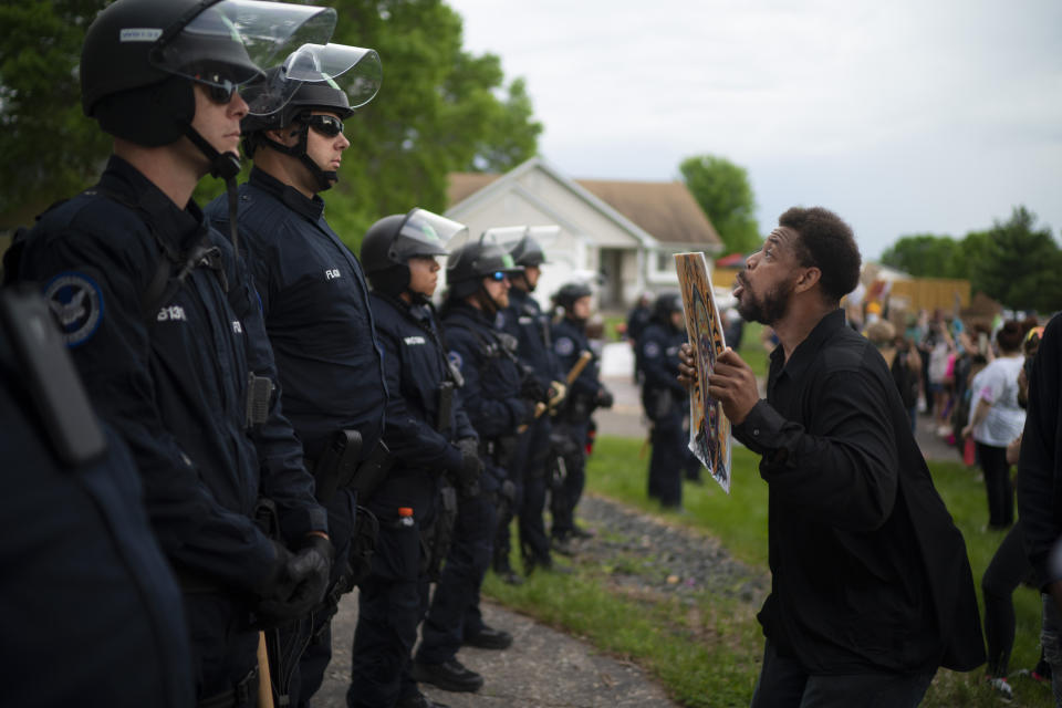 A demonstrator holding a sign jumps up and down so police officers behind the front lines could see it, outside the Oakdale, Minn,, home of fired Minneapolis police Officer Derek Chauvin on Wednesday evening, May 27, 2020. The mayor of Minneapolis called Wednesday for criminal charges against the white police officer seen on video kneeling against the neck of Floyd George, a handcuffed black man who complained that he could not breathe and died in police custody. (Jeff Wheeler/Star Tribune via AP)