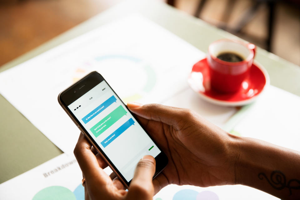 Person holding a smartphone with text messages on screen above a table with documents and a coffee cup