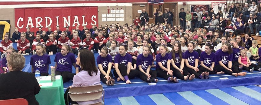 The teams at Saturday's Stick It for a Cure Gymnastics Invite listen to the guest speakers discussing the importance of the event and what it does for the community