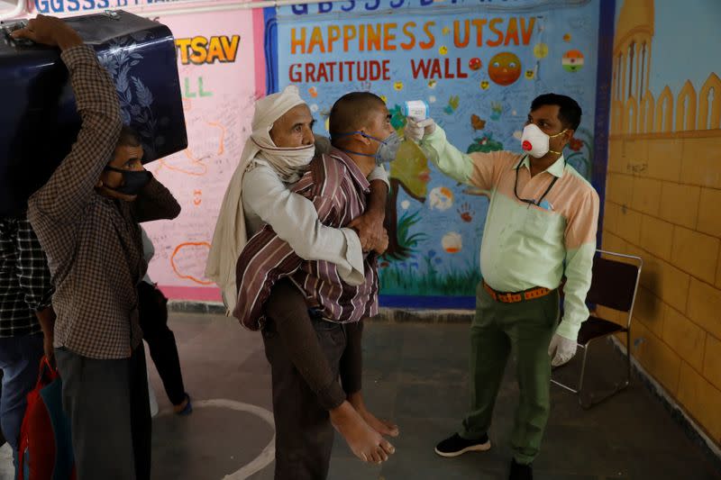 Un trabajador lleva a su padre a la espalda se hace controlar la temperatura antes de inscribirse en un tren hacia su estado natal de Uttar Pradesh, en Nueva Delhi, India, el 26 de mayo de 2020