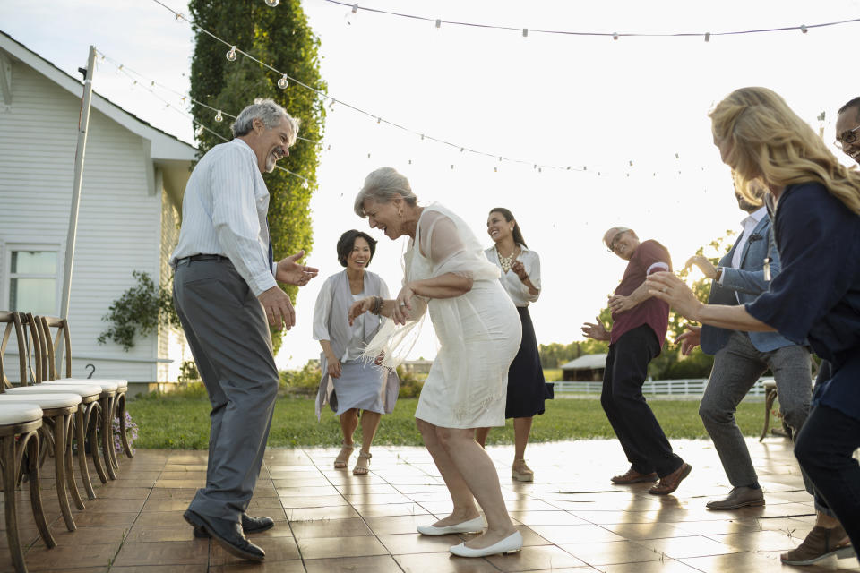 Friends dancing with senior bride and groom at wedding reception in rural garden