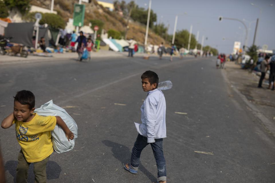 A boy carries a plastic bag as migrants gather on the roadside near Mytilene town, on the northeastern island of Lesbos, Greece, Tuesday, Sept. 15, 2020. Just over 6% of the 12,500 people left homeless last week by the fire that destroyed Greece's biggest camp for refugees and migrants have been rehoused in a new temporary facility under construction on the island of Lesbos. (AP Photo/Petros Giannakouris)