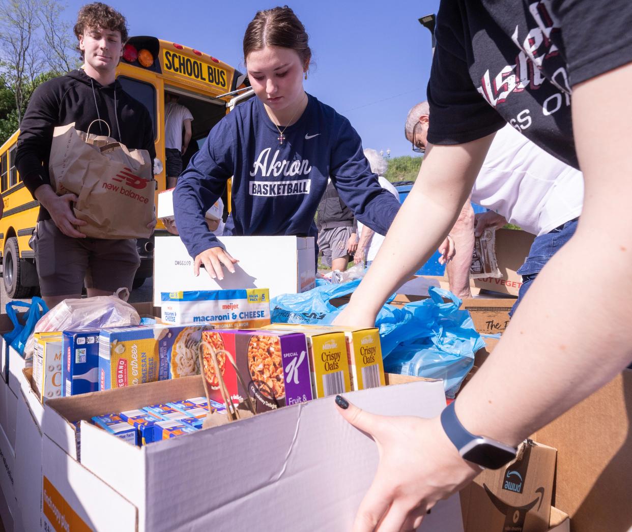 Walsh Jesuit High School seniors Grace Haines, center, and Noah Brock, left, help unload a Jackson Local school bus at the Akron-Canton Regional Foodbank's Stark County campus Tuesday in Canton. Volunteers helped unload food as part of the seventh annual "Hunger: The Bus Stops Here" fundraising drive.