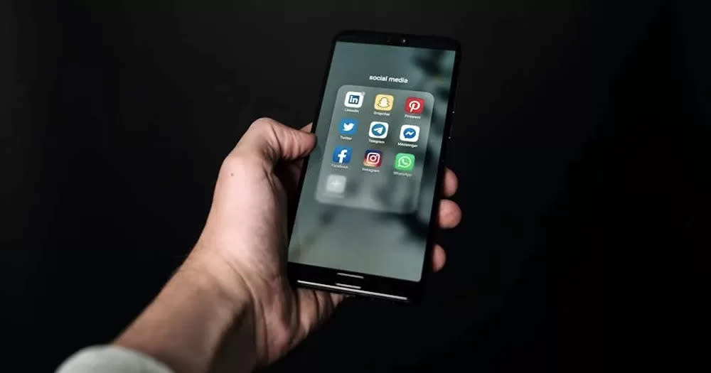 Photo of hand holding a phone with social media apps, which the Irish public wants to see more regulated, on the screen, with a dark background.