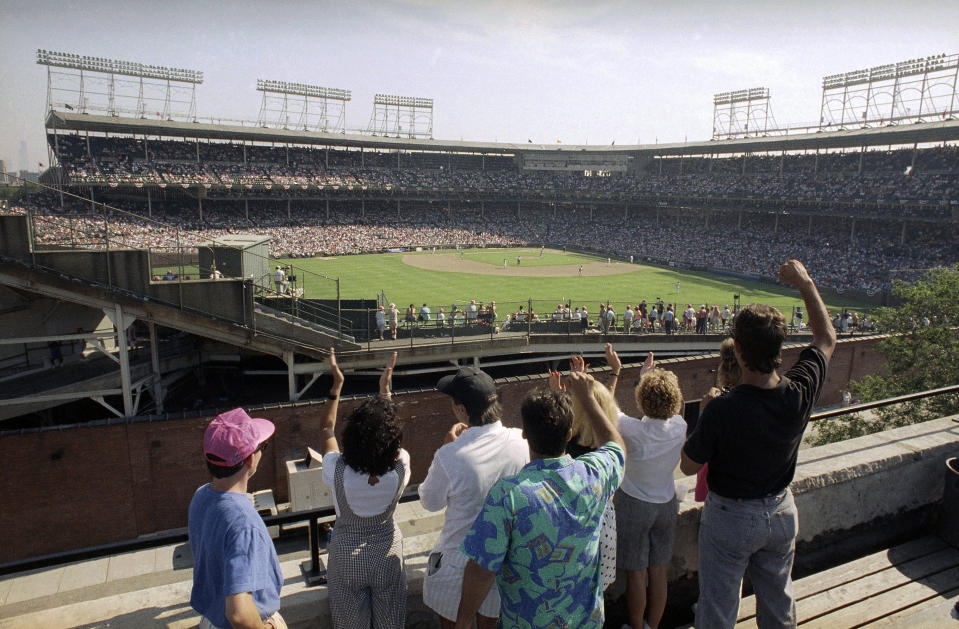 FILE - In this Monday, July 9, 1990, file photo, spectators watch an All-Star Game practice session from the roof of a building just outside Chicago's Wrigley Field. This week, Major League Baseball players and owners reached an agreement to play an abbreviated, 60-game season that would start July 23 or 24 in teams’ home ballparks. But the seats will be empty. Instead, fans hoping to see a game in person will be have to settle for pressing their faces up against hotel windows, squinting through metal grates or climb to rooftops when baseball returns this month in otherwise empty stadiums. (AP Photo/Seth Perlman, File)