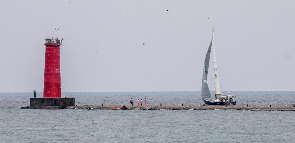 People walk on the north pier and a sailboat takes to Lake Michigan, Wednesday, July 28, 2021, in Sheboygan, Wis.