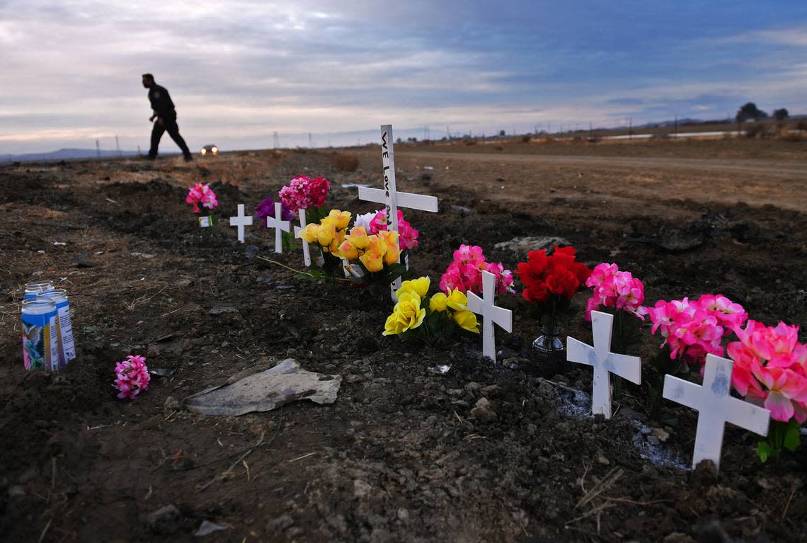 Seven small crosses and one large one form a memorial along Highway 33 as California Highway Patrol officers survey the scene Saturday, Jan. 2, 2021, a day after Friday’s night’s head-on crash that killed nine, including seven children, south of Coalinga, California.