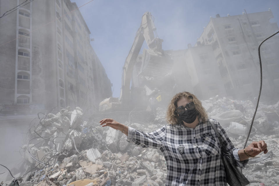 Pedestrians pass through clouds of dust as heavy construction equipment is used to sift through rubble to uncover valuables before it is transported away from the scene of a building destroyed in an airstrike prior to a cease-fire that halted an 11-day war between Gaza's Hamas rulers and Israel, Thursday, May 27, 2021, in Gaza City. (AP Photo/John Minchillo)