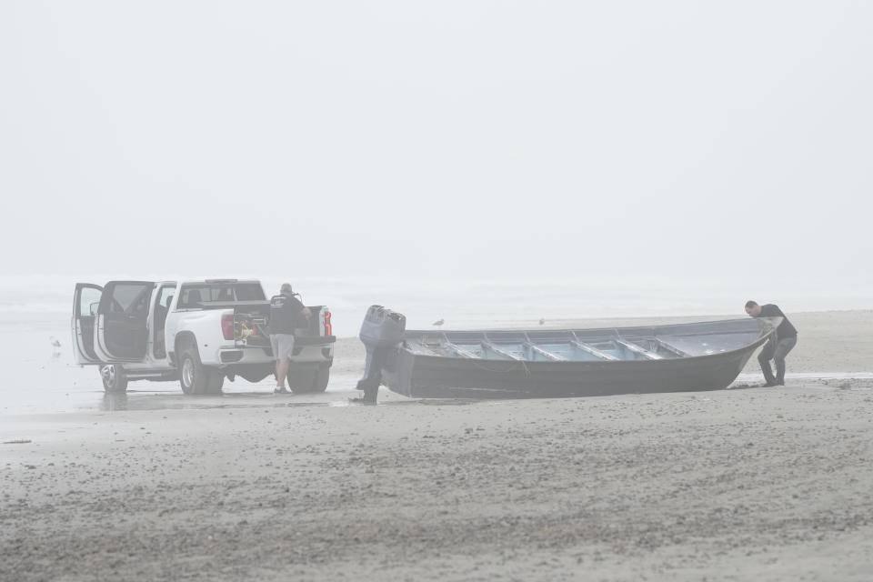 Boat salvager Robert Butler, left, and KC Ivers, right, prepare to move one of two boats on Blacks Beach, Sunday, March 12, 2023, in San Diego. Authorities say multiple people were killed when two suspected smuggling boats overturned off the coast in San Diego, and crews were searching for additional victims. (AP Photo/Gregory Bull)