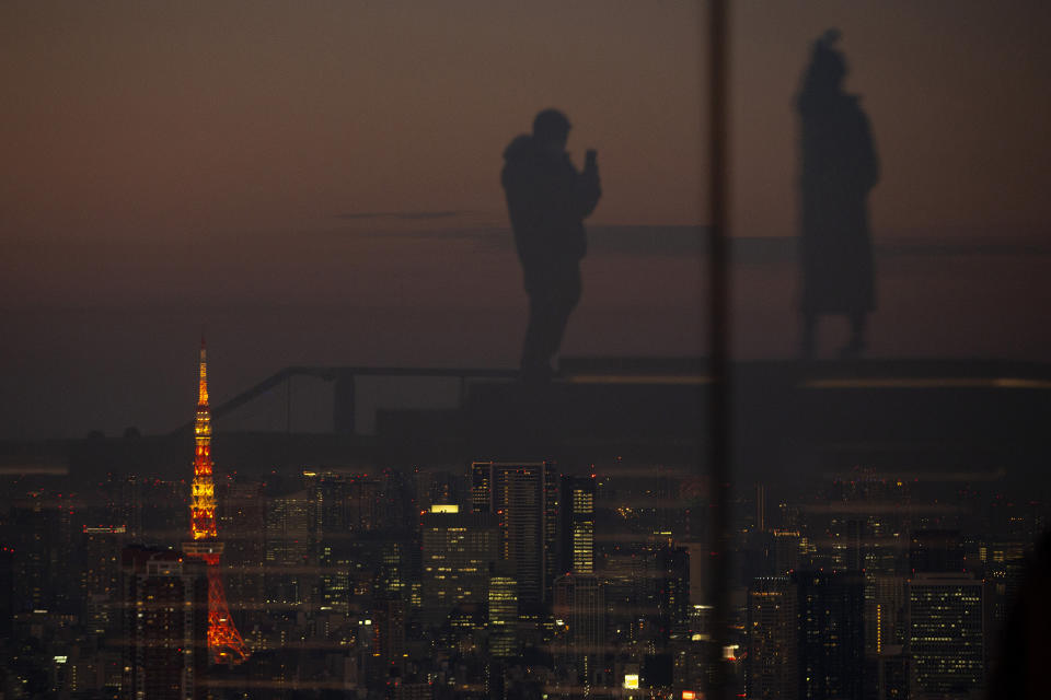 Silhouetted against the warm sunset skyline and the illuminated Tokyo Tower, visitors are reflected on the glass walls of a rooftop observation deck Thursday, Jan. 21, 2021, in Tokyo. (AP Photo/Kiichiro Sato)