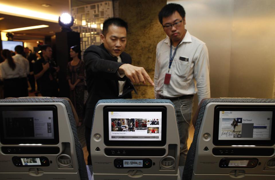 A Singapore Airlines staff member points out to the features on a row of economy class seats during the launch of their new generation of cabin products at Changi Airport in Singapore July 9, 2013. The new seats and in-flight entertainment system, an investment of nearly $150 million by the company, will be rolled out from September, starting with flights between Singapore and London on eight Boeing 777-300ER aircrafts. REUTERS/Edgar Su (SINGAPORE - Tags: TRANSPORT BUSINESS)