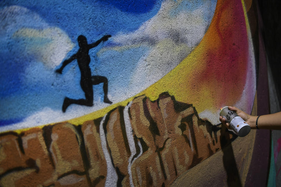 Street artist Wolfgang Salazar works on his most recent mural in the Boleita neighborhood of Caracas, Venezuela, Tuesday, Jan. 5, 2021. The mural depicts triple-jump indoor world record setter Yulimar Rojas’ smiling face above an image of her silhouette leaping Venezuela's iconic Angel Falls, the world’s highest waterfall. (AP Photo/Matias Delacroix)