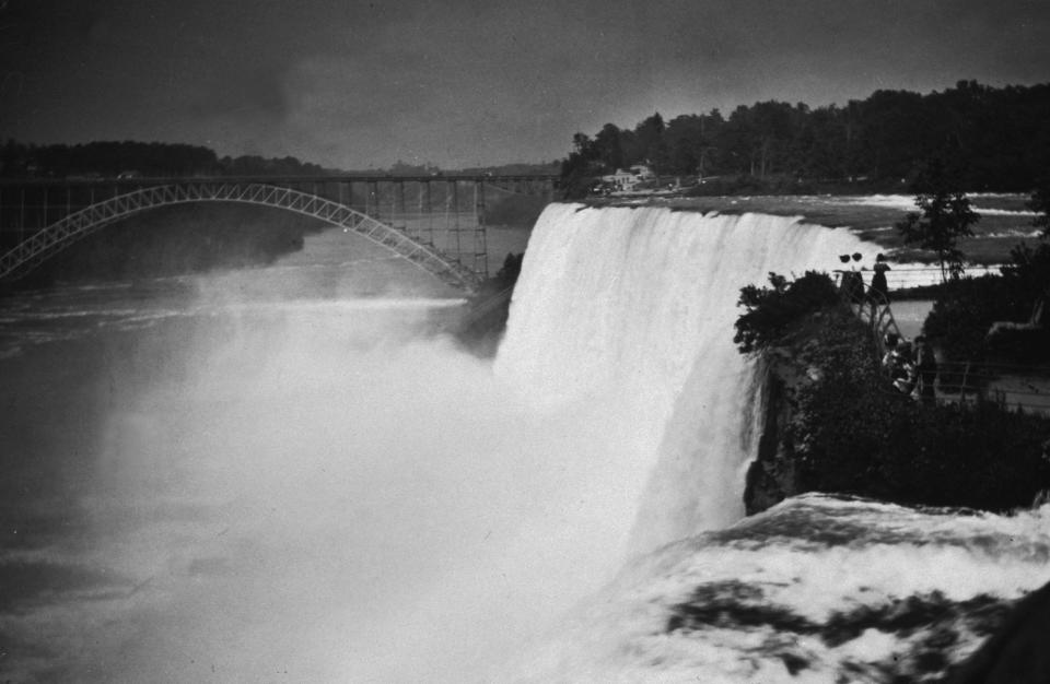Spectators observe the American Falls and steel arch bridge from Goat Island, Niagara Falls, New York in 1895.