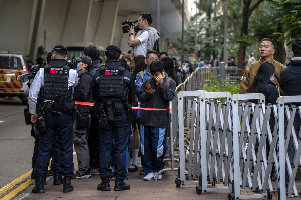 Policemen stand guard as they keep a watchful eye on people gathered in a cordoned off area as a vehicle believed to be carrying Jimmy Lai arrives at West Kowloon Magistrates' Courts, where Lai's trial is scheduled to open, in Hong Kong, Monday, Dec. 18, 2023. (AP Photo/Vernon Yuen)