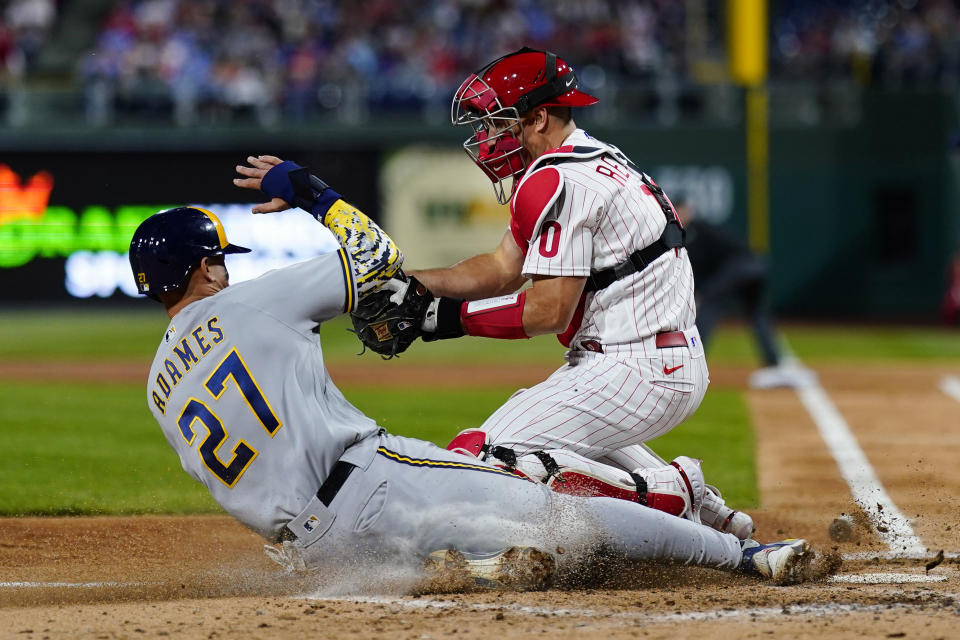 Milwaukee Brewers' Willy Adames, left, scores past Philadelphia Phillies catcher J.T. Realmuto on a sacrifice fly by Milwaukee Brewers' Hunter Renfroe during the third inning of a baseball game, Friday, April 22, 2022, in Philadelphia. (AP Photo/Matt Slocum)