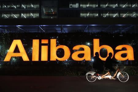 People ride a double bicycle past a logo of The Alibaba Group at the company's headquarters on the outskirts of Hangzhou, Zhejiang province November 10, 2014. REUTERS/Aly Song (CHINA - Tags: BUSINESS EMPLOYMENT LOGO) - RTR4DLN9