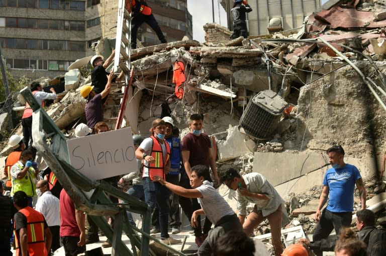 A placard reads "Silence" as rescuers hurry to free possible victims out of the rubble of a collapsed building in Mexico City