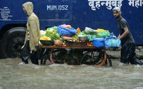 Indian vegetable vendors push their cart along a flooded street during heavy rain showers in Mumbai - Credit: Punit Paranjpe/AFP