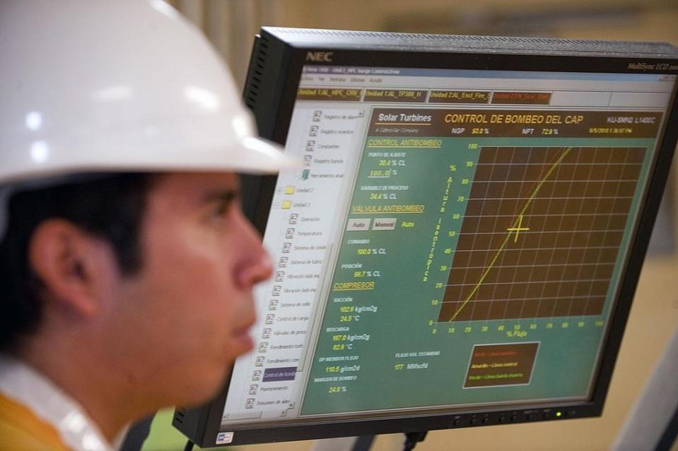 Un trabajador con casco pasa delante de una pantalla