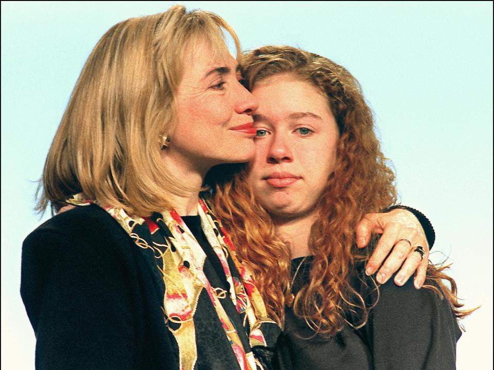 a young hillary clinton and chelsea clinton in january 1933. hillary is holding her daughter close to her chest with a smile on her face, while a young chelsea is standing with a neutral expression