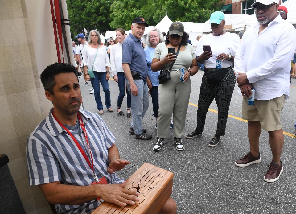 Artisphere 2023 in downtown Greenville showcased music and artists in the city's downtown area. This is Artisphere on May 13, 2023. This is wood art by Adam Crowell.  Crowell, left, play for guests on one of his wood art pieces. 