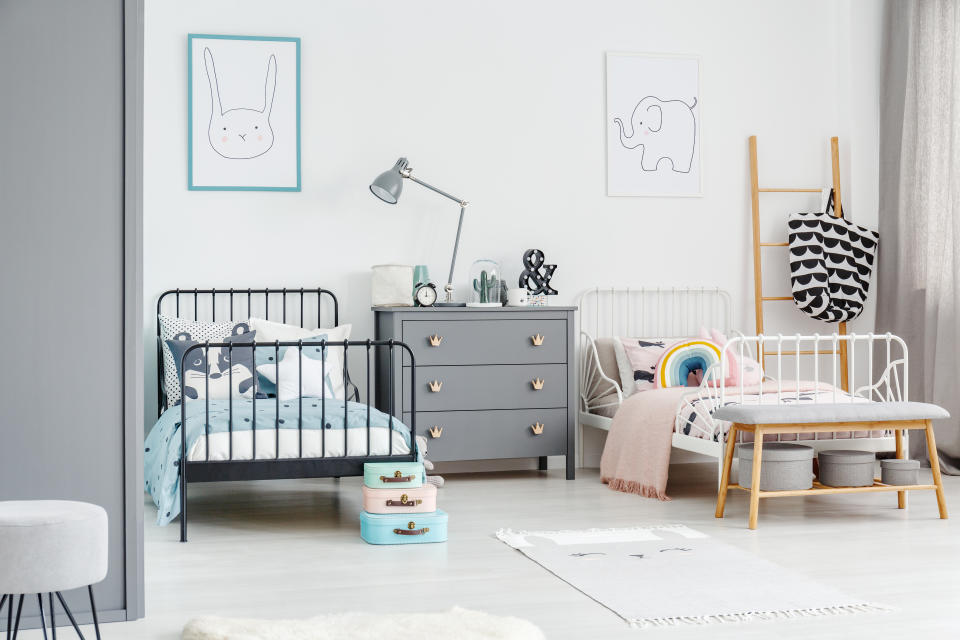 White bed for a girl and black one for a boy in a siblings  bedroom interior with posters of a rabbit and an elephant on a white wall. Simple scandi design. Real photo