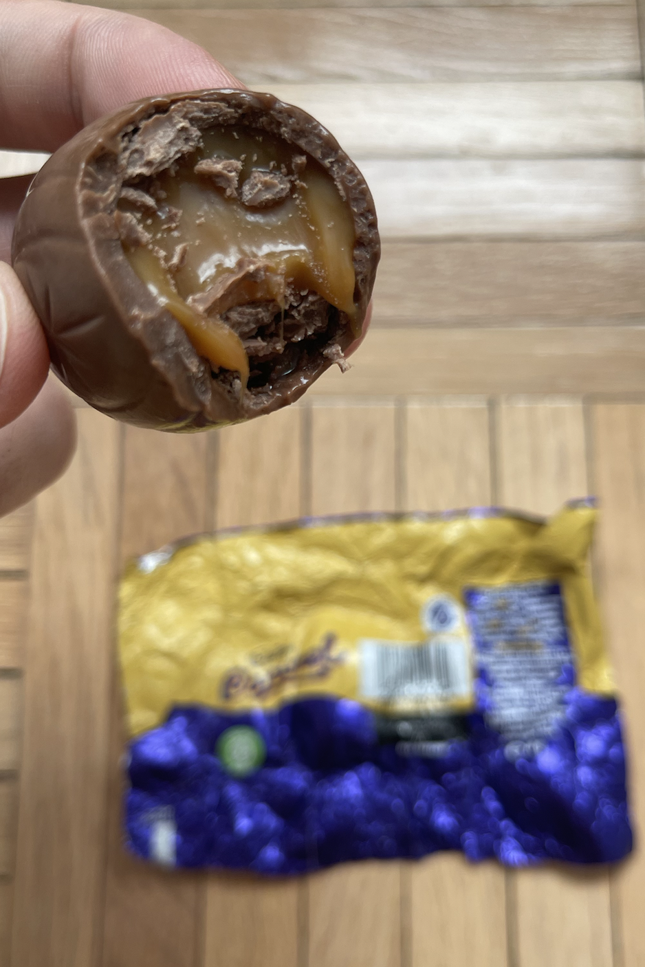 Person holding a bitten chocolate with caramel filling above its wrapper