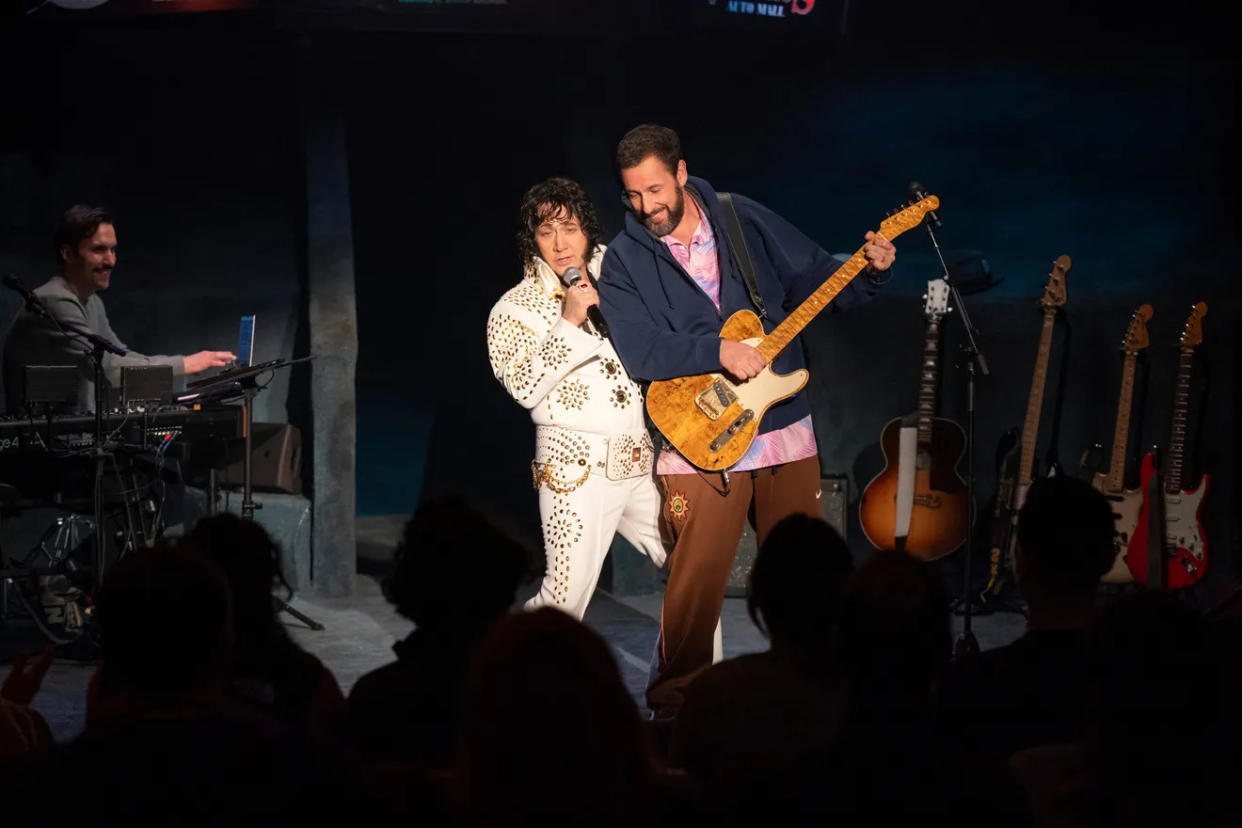 Adam Sandler, holding a guitar, performs with Rob Schneider during his stand-up special.