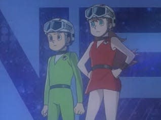 two young people in futuristic outfits and helmets standing on a cliffside