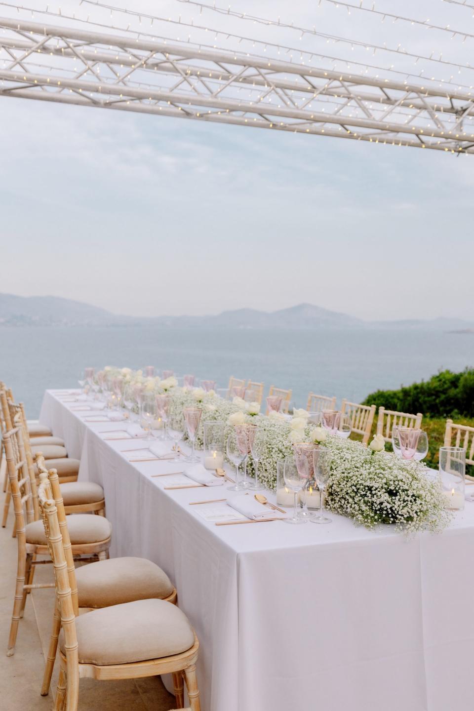 A table covered in flowers overlooks the ocean and mountains.