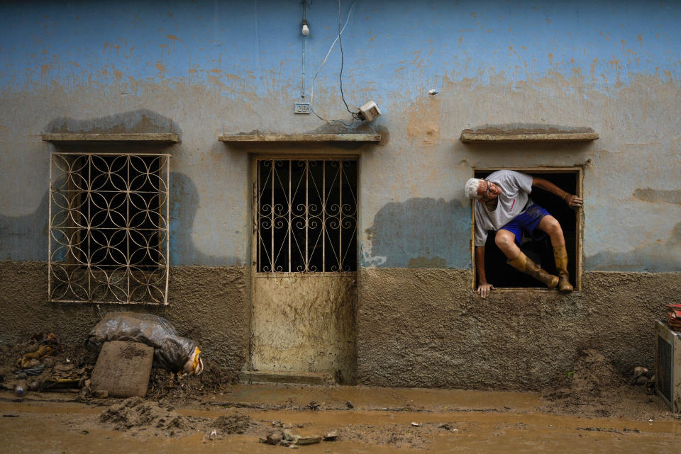 Jose Medina jumps out his home flooded by the overflow of a ravine caused by intense rains in Las Tejerias, Venezuela, Sunday, Oct. 9, 2022. (AP Photo/Matias Delacroix)